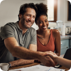 A couple smiles as the husband shakes their independent agent’s hand. 